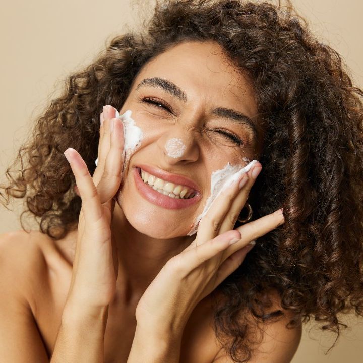 mujer sonriente aplicándose crema en la cara